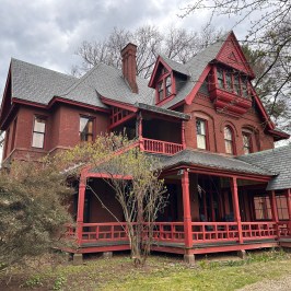 Large red Victorian-style house with detailed trim and covered porch, surrounded by trees.
