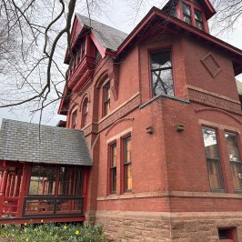 Red brick Victorian-style house with ornate details and a small porch.