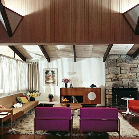 Mid-century modern living room with wooden ceiling, stone fireplace, and colorful furniture.