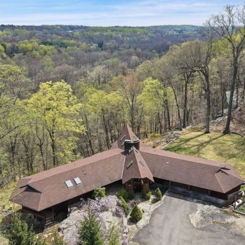 Aerial view of a unique brown-roofed house surrounded by trees and forest.