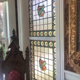 Decorative stained glass windows with shields above an ornate wooden chair.
