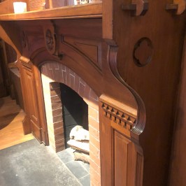 Ornate wooden fireplace with brick interior and logs, partial view of a person wearing shorts.