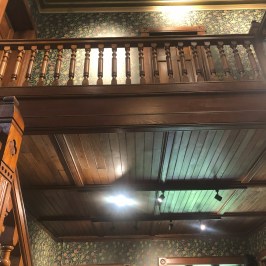 Vintage interior with wooden banister and floral wallpaper, featuring wooden doors and ceiling.
