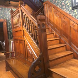 Wooden staircase with detailed railing and ornate wallpaper on walls.