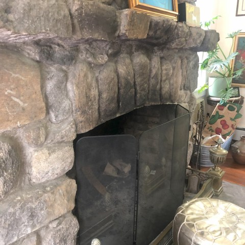 Stone fireplace with a screen, gold decor, and a framed picture on the mantel.