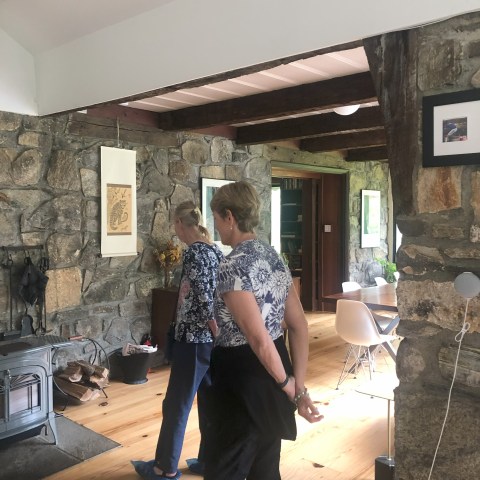Two people in a rustic living room with stone walls and wooden floors, near a wood stove.