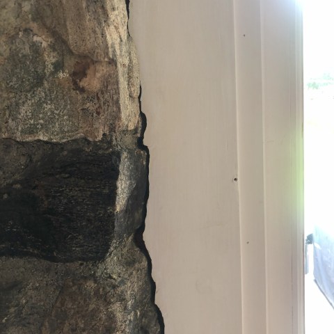 Close-up of stone wall meeting white interior wall with a visible gap.