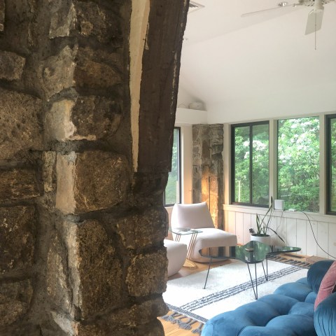 Stone archway leading to a sunlit room with modern blue seating and large windows.