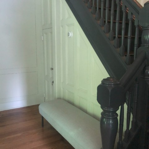 Cozy nook under dark wood stairs with light bench and wood floor.