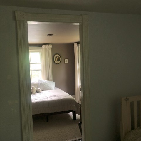 View through doorway into cozy bedroom with bed, pillows, and wall art.