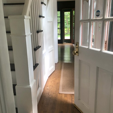 Open door revealing a hallway with stairs and a view to the outside through a glass door.