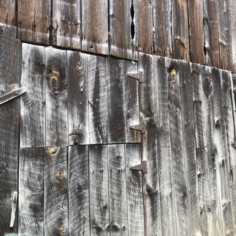 Weathered wooden barn wall with visible knots and rusty metal hinges.