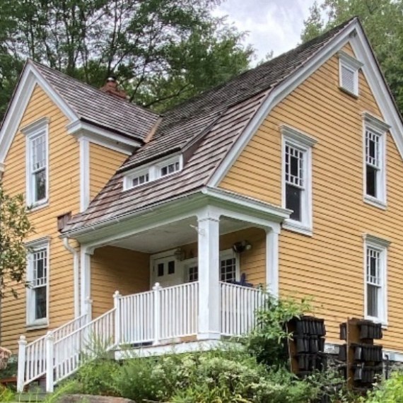 Yellow two-story house with white trim, surrounded by trees and bushes.