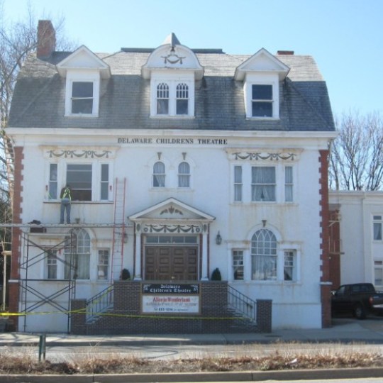 Facade of a large historic building labeled 'Delaware Children's Theatre' with scaffolding and caution tape.