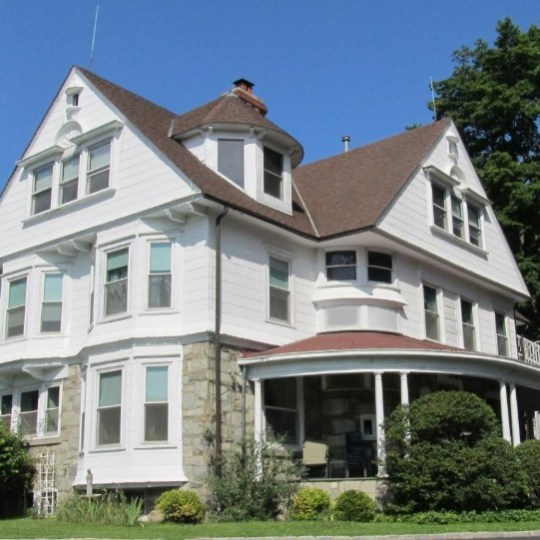 Large white Victorian-style house with brown roof and front porch.
