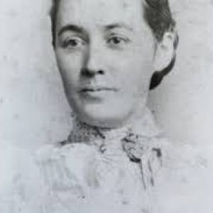 Black and white portrait of a woman in a high-collared dress with hair tied back.