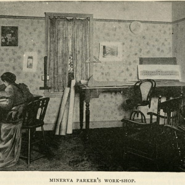 A woman works at a desk in a vintage-style office with chairs and architectural plans.