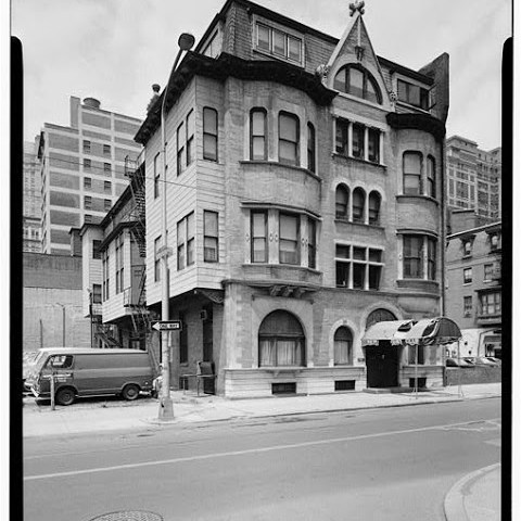 Historic three-story stone building on a city street corner with arched windows and mansard roof.