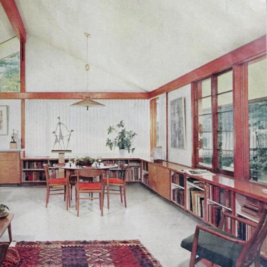 Mid-century modern room with table, chairs, bookshelf, and colorful rug.