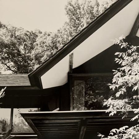 Black and white photo of a house with pitched roof and large trees in the background.