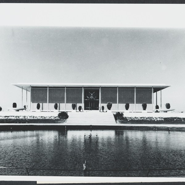 Symmetrical modernist building with large pool and stairs in front, under a clear sky.
