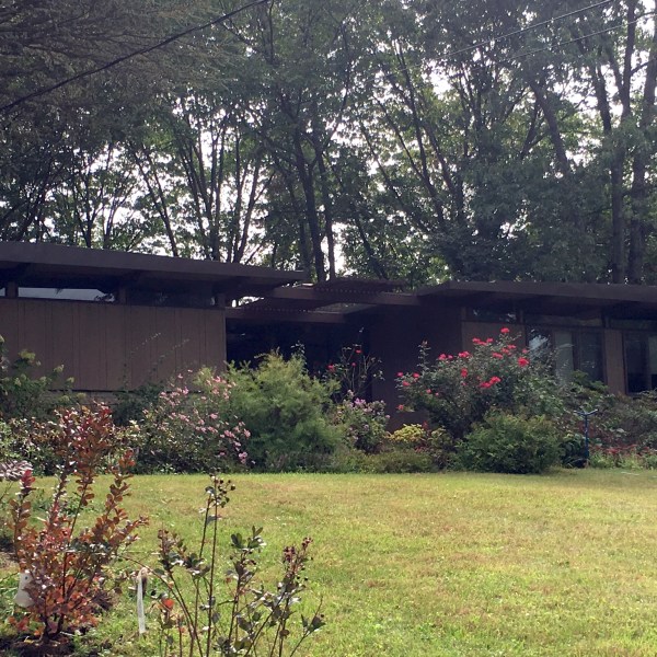 Mid-century modern house with large windows, surrounded by trees and garden.