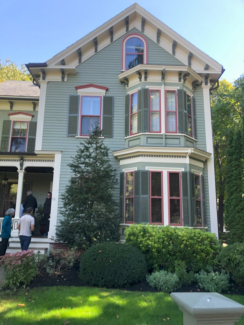 Victorian-style house with green siding, red trim, and people on porch.