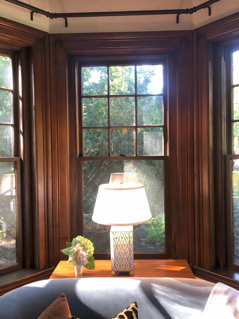 Cozy interior with lamp on wooden table by windows, flowers and couch.