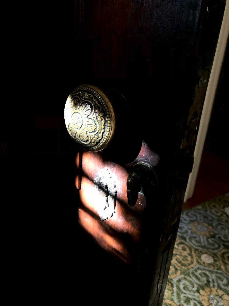 Ornate brass doorknob on a wooden door, lit by dramatic sunlight.