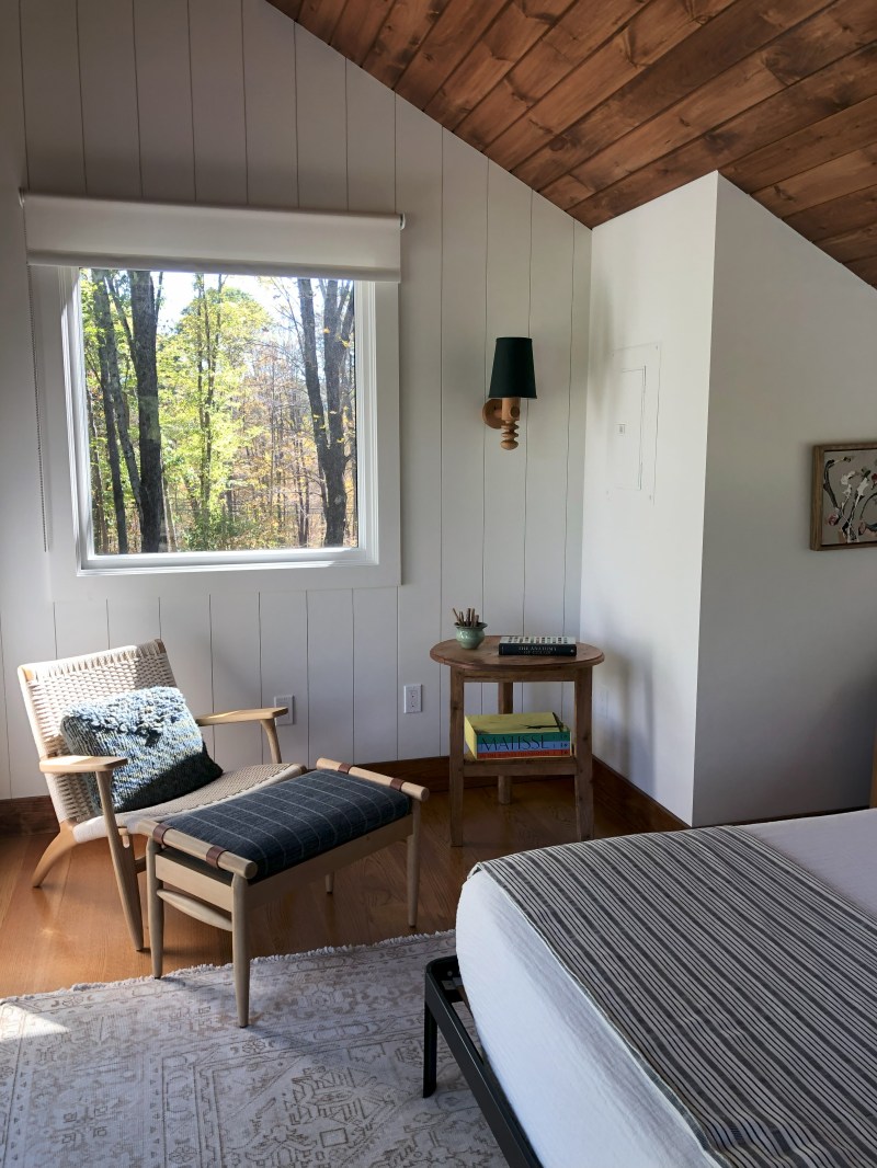 Cozy bedroom corner with chair, ottoman, and window view of trees.
