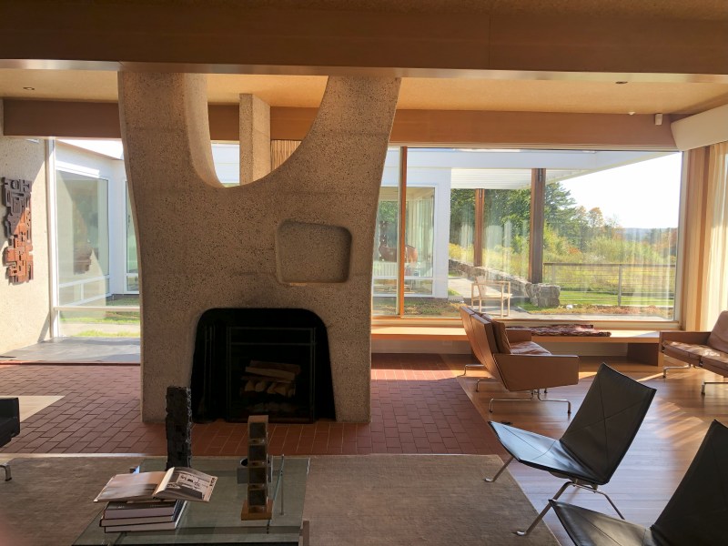 Modern living room with large windows, unique fireplace, chairs, and a view of the garden outside.