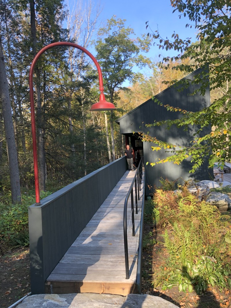 Wooden ramp with railing leading to a dark building, surrounded by trees and foliage.