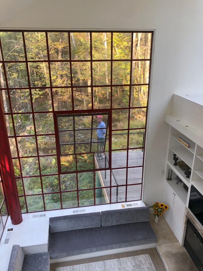 Large window view with a person outside, modern interior with gray sofa and sunflowers in vase.