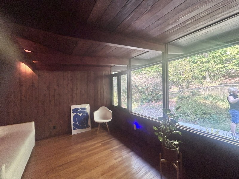 Wood-paneled room with large windows, chair, art print, and plant.