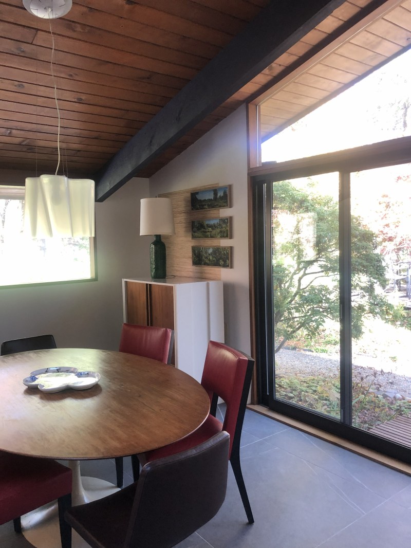Dining area with wooden table, red chairs, large window, and wooden ceiling.