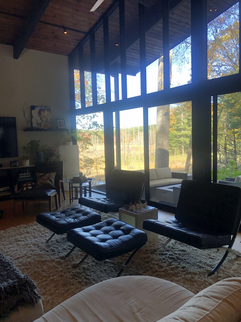 Spacious living room with large windows, black chairs, and outdoor view of trees.