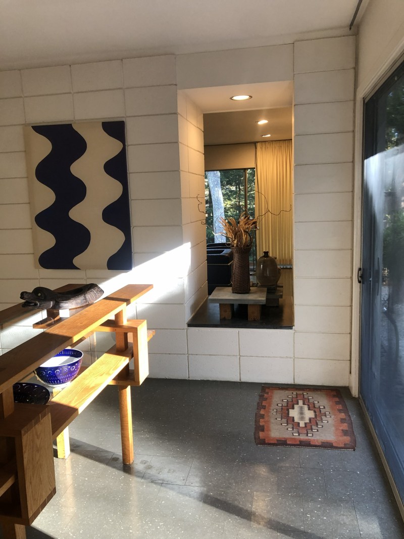 Sunlit room with abstract art on wall, wooden shelf, and rug on tiled floor.