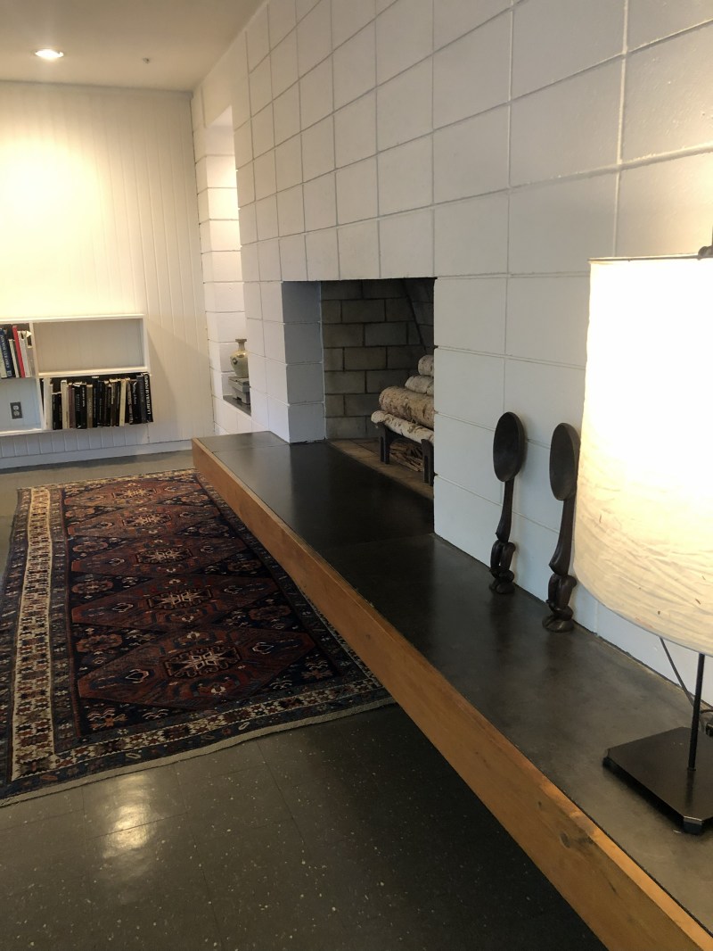 Cozy room with fireplace, rug, bookshelf, and soft lighting from a lamp.