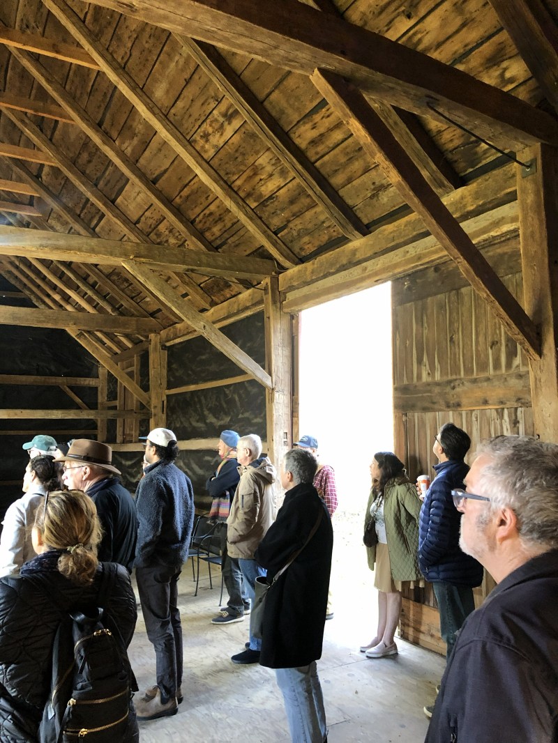 A group of people standing inside a wooden barn, looking towards an open doorway.