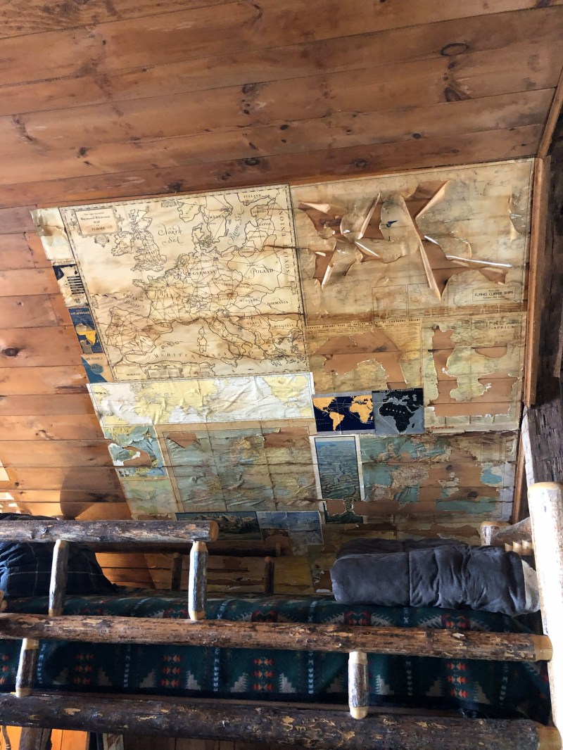 Wooden ceiling with old map pieces and a bunk bed in a rustic room.