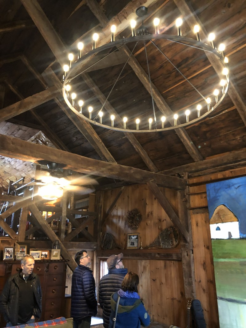 People in a rustic room with a large circular chandelier and wooden beams.