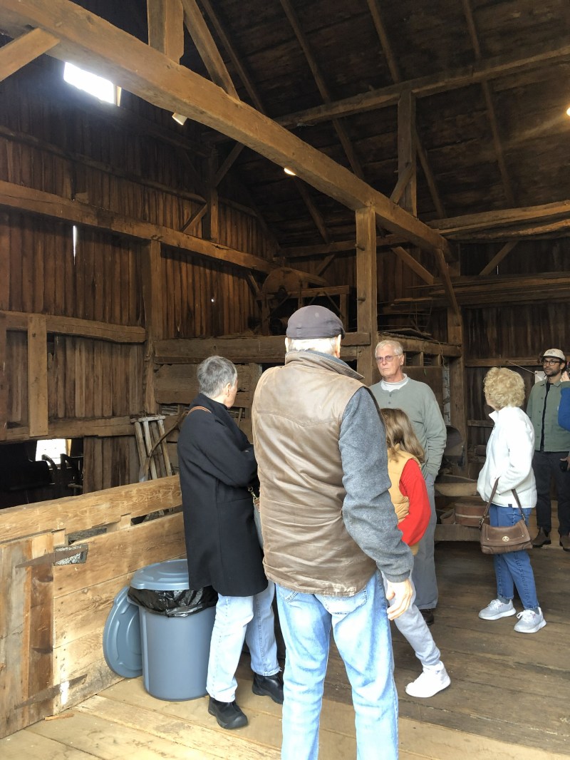 People standing inside a wooden barn with beams and a trash can visible.