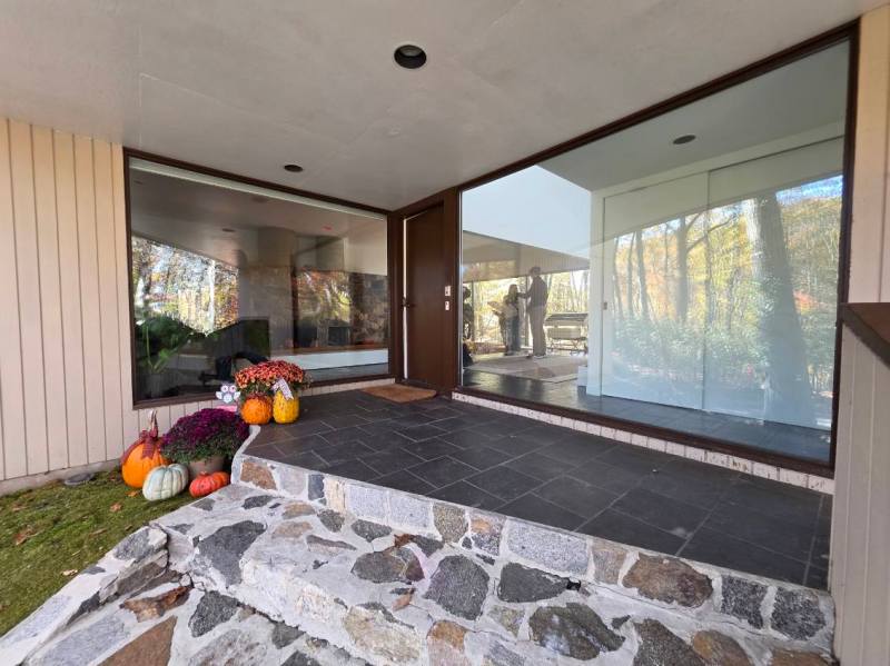 Entrance with pumpkins and flowers, large glass windows, and a stone path.
