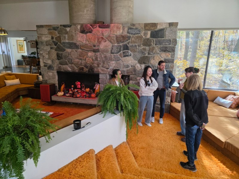 Group of people chatting in a cozy living room with stone fireplace and orange carpet.