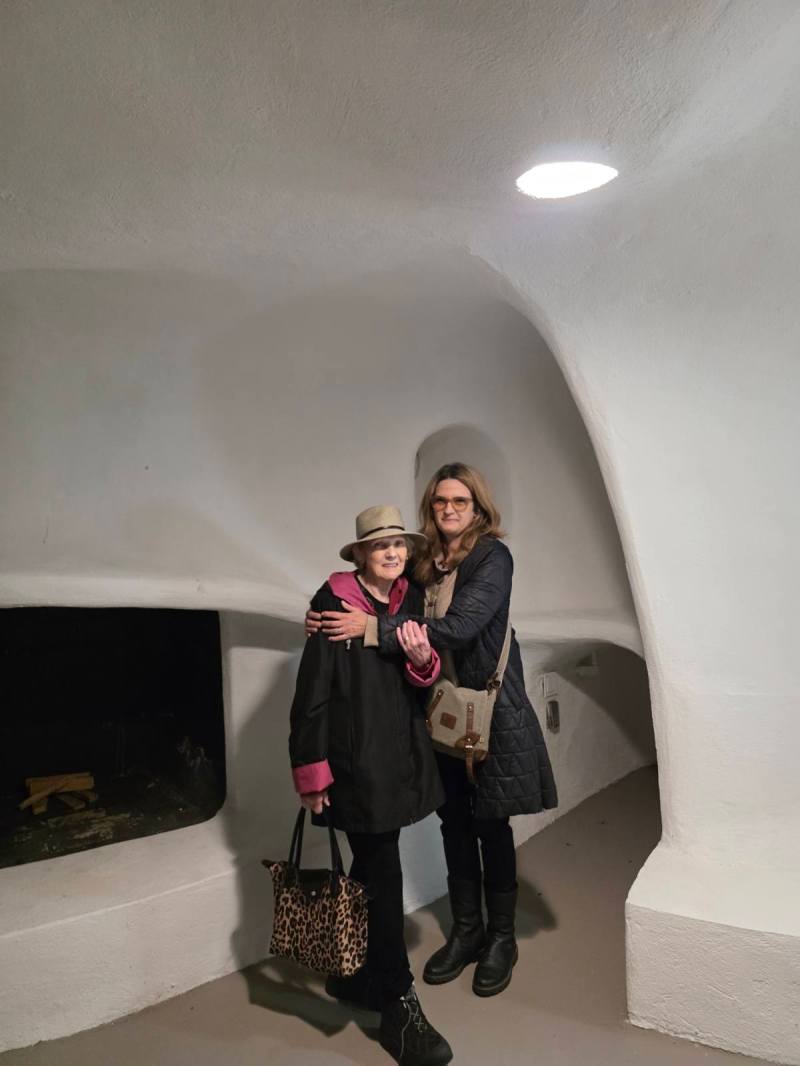 Two women standing in a white, curved room with a small fireplace.