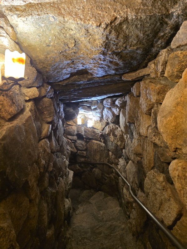 Stone-walled tunnel with dim lighting and a metal handrail on the right.