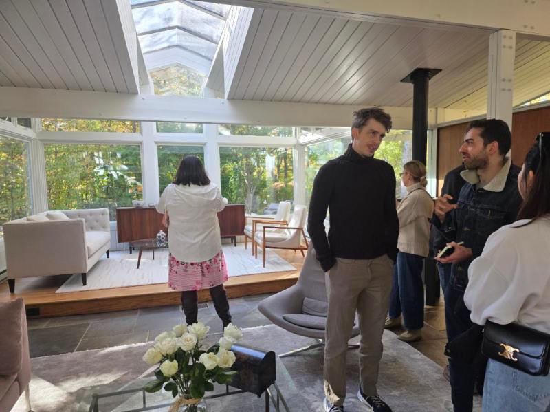 People conversing in a bright room with large windows and modern furniture.