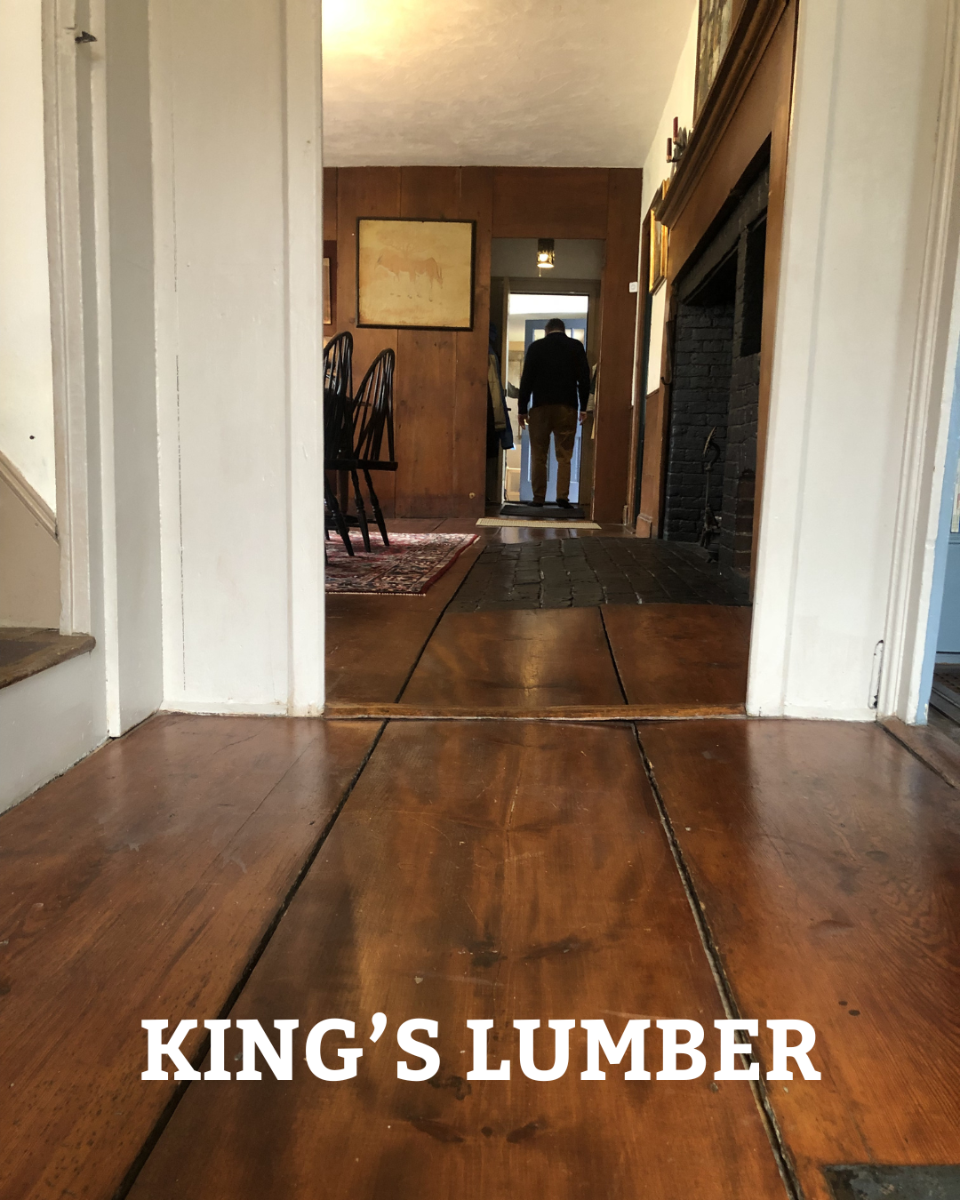 Wooden floor hallway leading to front door with chairs and wall art.